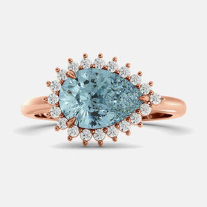 Rose gold ring with a large blue gemstone and smaller diamonds on a light gray background
