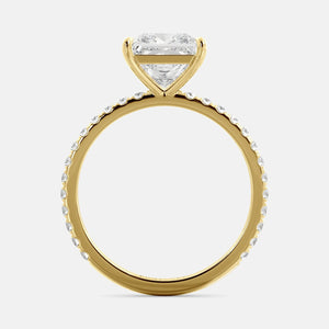 A close-up of a yellow gold cushion solitaire lab-grown diamond ring with an eternity band. The lab-grown diamond is a climate -positive diamond, created by using carbon from the atmosphere. The ring is set with a 1-carat cushion-cut diamond in the center, surrounded by a row of smaller diamonds on the band. The ring is available in a variety of sizes and starts at \\$6,400.00.
