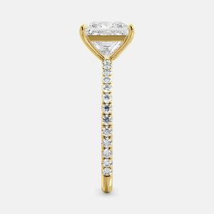 A close-up of a yellow gold cushion solitaire lab-grown diamond ring with an eternity band. The lab-grown diamond is a climate -positive diamond, created by using carbon from the atmosphere. The ring is set with a 1-carat cushion-cut diamond in the center, surrounded by a row of smaller diamonds on the band. The ring is available in a variety of sizes and starts at \\$6,400.00.