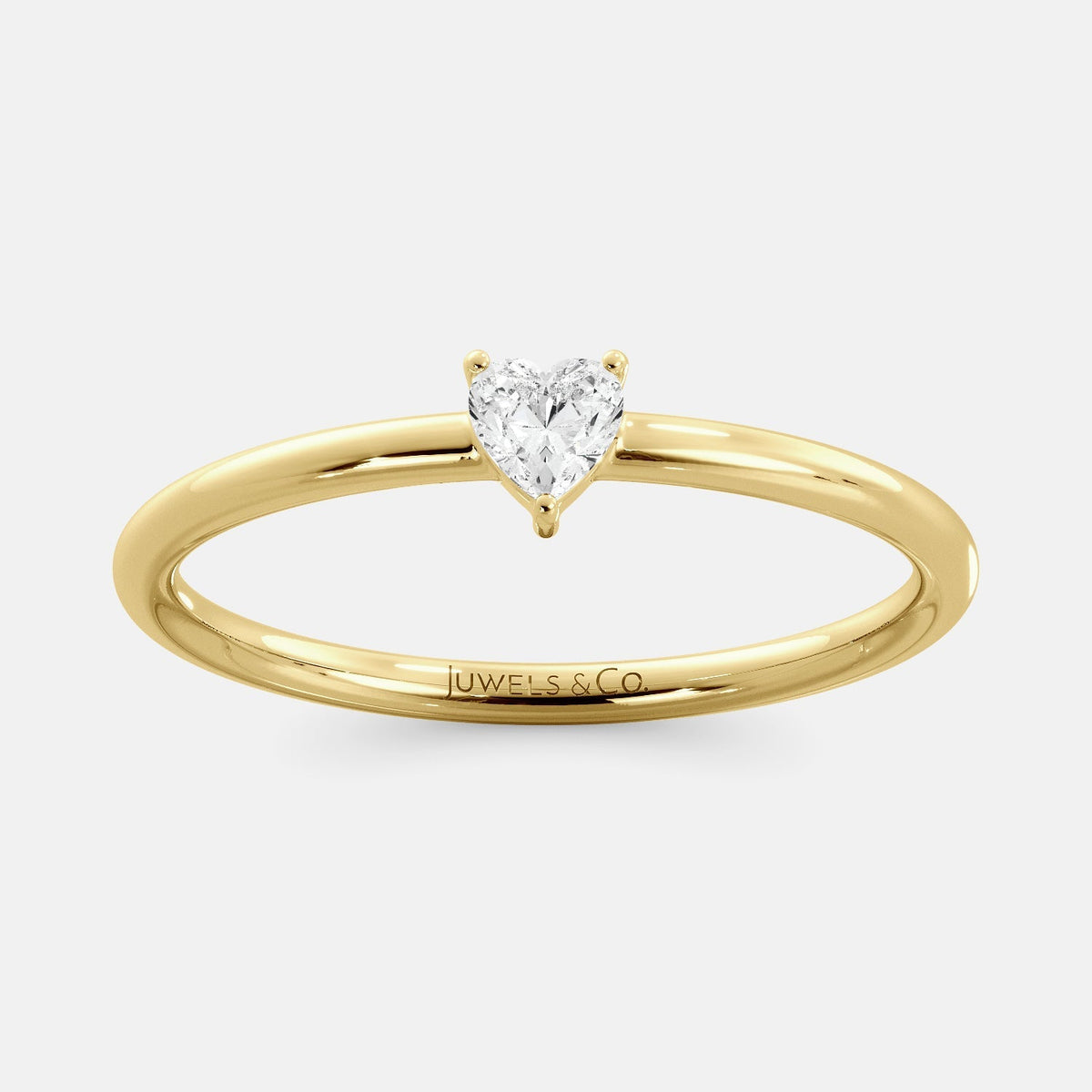 A close-up of a heart-shaped solitaire diamond ring in recycled yellow gold. The ring is set with a single, large diamond in the center of a heart-shaped setting. The ring is made of recycled yellow gold and has a simple, elegant design. The diamond is sparkling and reflects light beautifully. The ring is a perfect gift for a loved one or a special occasion.