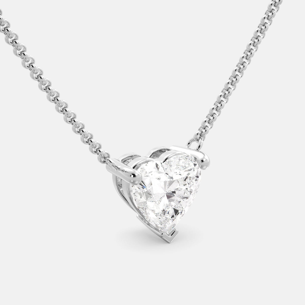 A close-up of a heart-shaped diamond necklace in recycled white gold. The necklace is set with a single heart-shaped diamond in the center of a pendant. The necklace is made of recycled white gold and has a simple, elegant design. The diamond is sparkling and reflects light beautifully. The necklace is a perfect gift for a loved one or a special occasion.