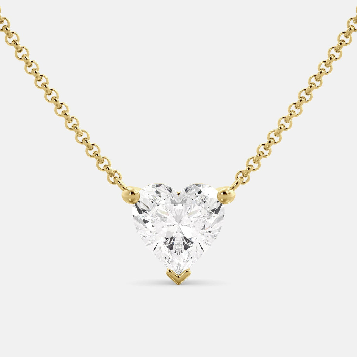 A close-up of a heart-shaped diamond necklace in recycled yellow gold. The necklace is set with a single heart-shaped diamond in the center of a pendant. The necklace is made of recycled yellow gold and has a simple, elegant design. The diamond is sparkling and reflects light beautifully. The necklace is a perfect gift for a loved one or a special occasion.