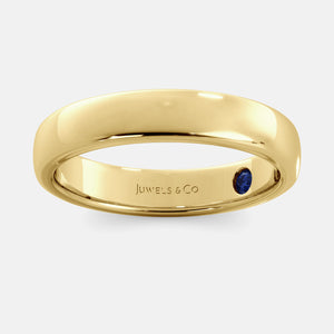 A close-up of a yellow gold flat wedding band with a hidden stone. The band is a classic and timeless design that is perfect for any occasion. The hidden stone can be customized with one of 12 different gemstones, including diamonds, rubies, sapphires, and emeralds. This makes the band a unique and personal choice for the wearer.