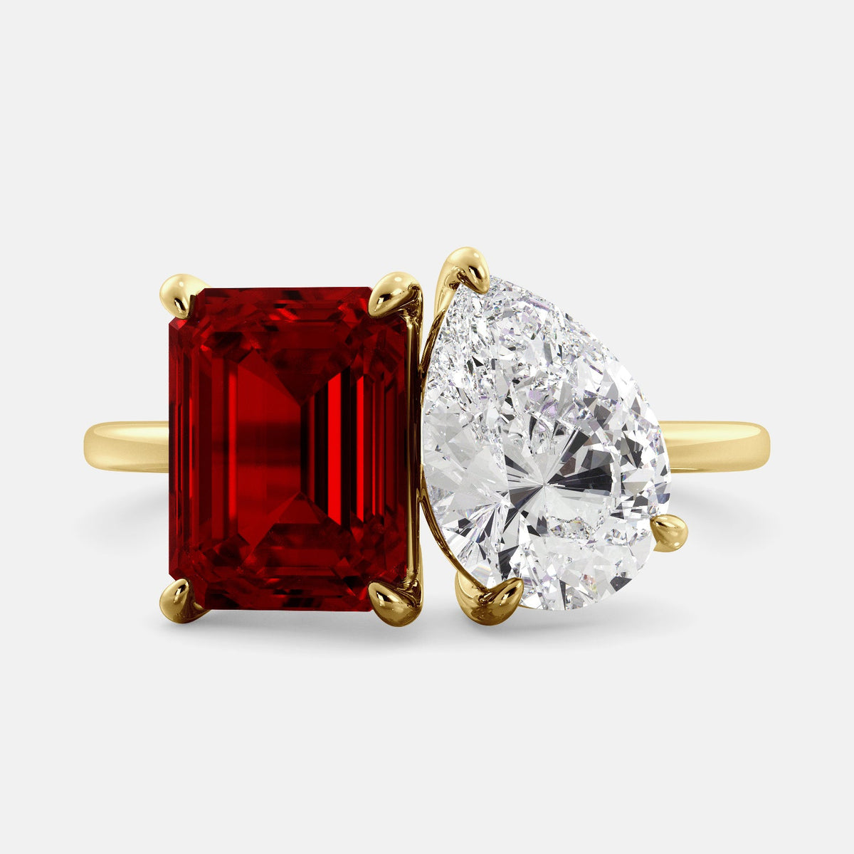 A toi et moi ring with an emerald-cut ruby and a pear-cut gemstone. The emerald-cut morganite is set on the left of the ring, and the pear-cut gemstone is set on the right. The ring is made of recycled yellow gold and has a simple, elegant design. The pear-cut gemstone can be customized. **Here are some additional details about the image:** * The emerald-cut white ruby is a birthstone for July. * The pear-cut gemstone can be customized to any stone of your choice.