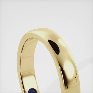 A close-up of a yellow gold flat wedding band with a hidden stone. The band is a classic and timeless design that is perfect for any occasion. The hidden stone can be customized with one of 12 different gemstones, including diamonds, rubies, sapphires, and emeralds. This makes the band a unique and personal choice for the wearer.