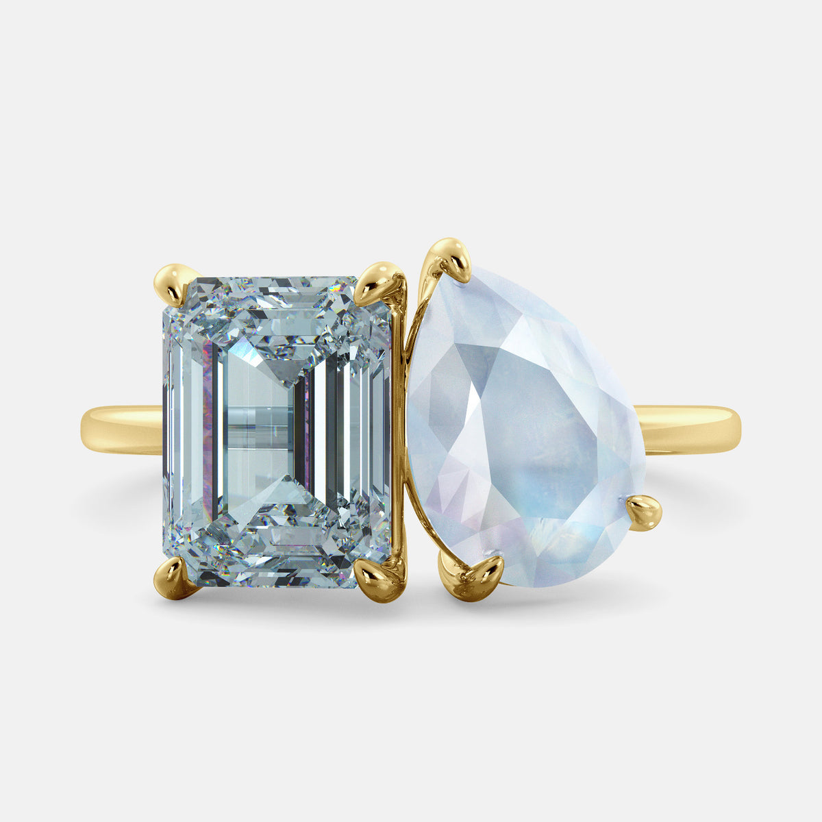A toi et moi ring with an emerald-cut aquamarine and a pear-cut gemstone. The emerald-cut morganite is set on the left of the ring, and the pear-cut gemstone is set on the right. The ring is made of recycled yellow gold and has a simple, elegant design. The pear-cut gemstone can be customized. **Here are some additional details about the image:** * The emerald-cut aquamarine is a birthstone for March. * The pear-cut gemstone can be customized to any stone of your choice.
