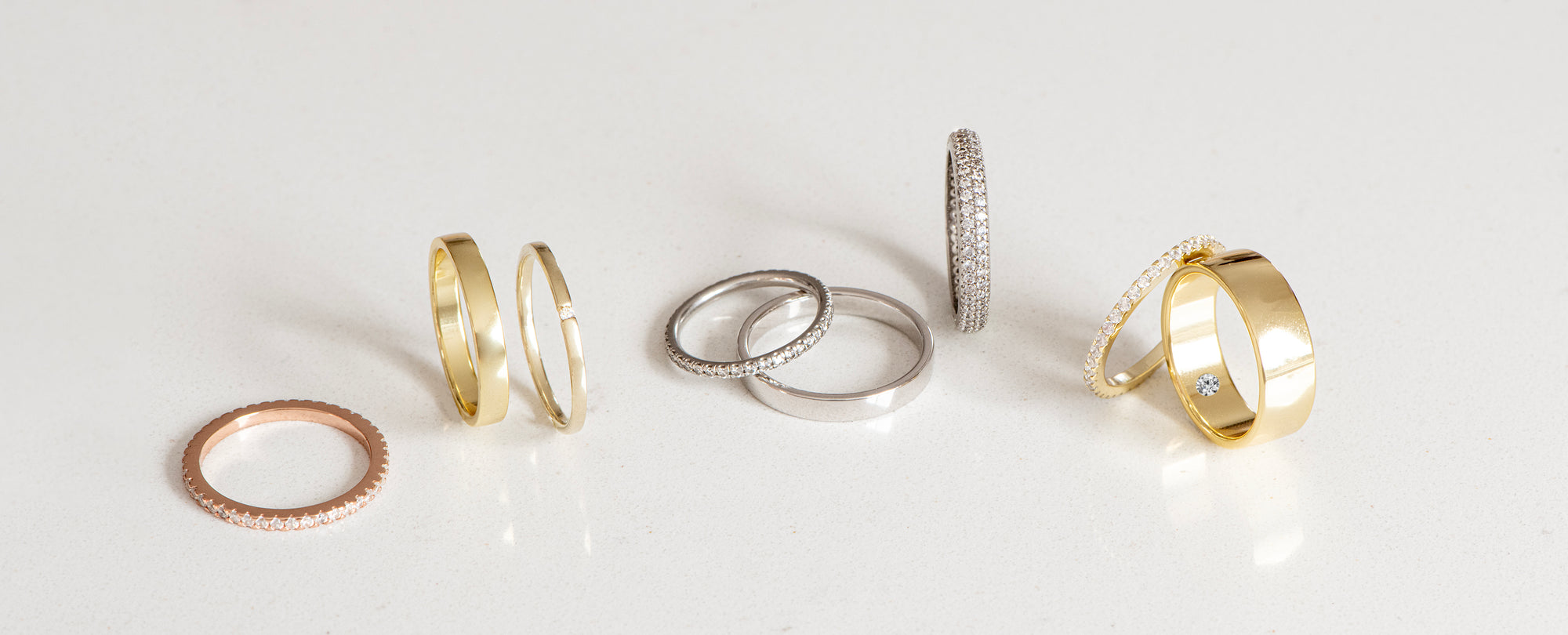 A close-up of a selection of wedding bands on a white background. The bands are made of 14K gold. They are also set with different stones, including diamonds, rubies, and sapphires. The bands are all different styles, from simple bands to more elaborate designs. The image is both beautiful and elegant, and it is sure to inspire couples who are looking for wedding bands.