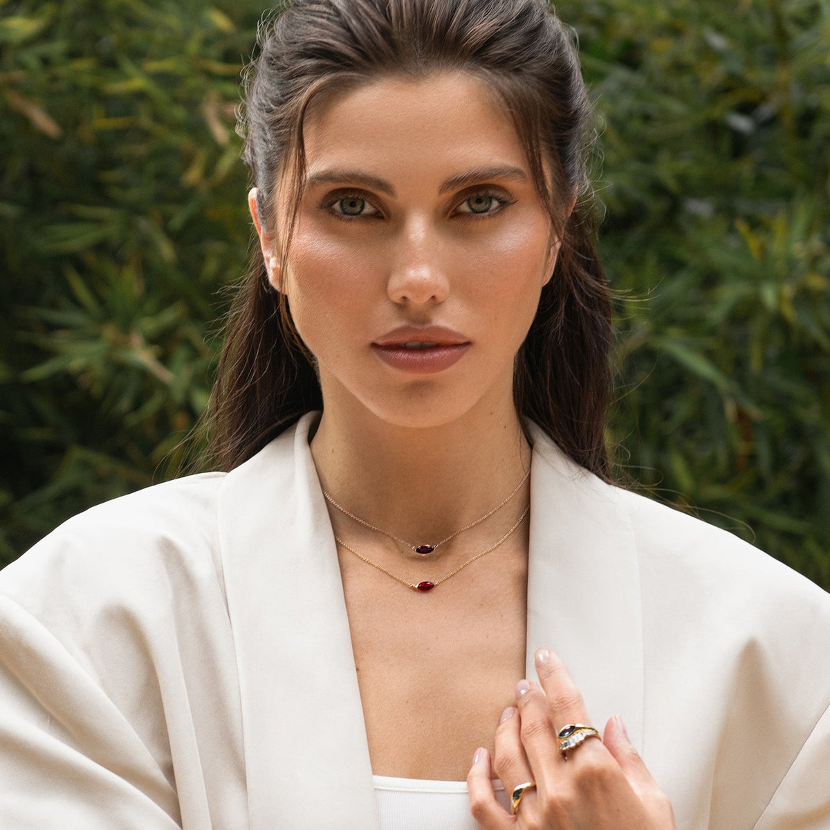 Woman wearing a white outfit with jewelry against a green foliage background