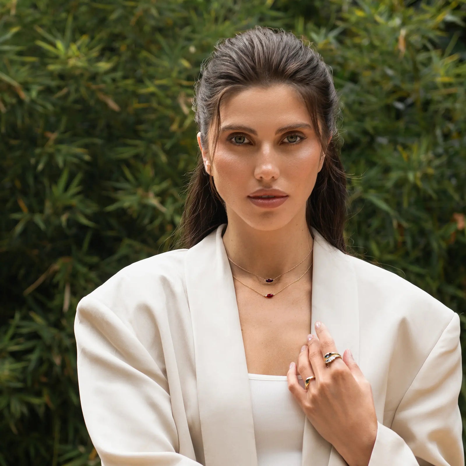 Woman wearing a white outfit with jewelry against a green foliage background