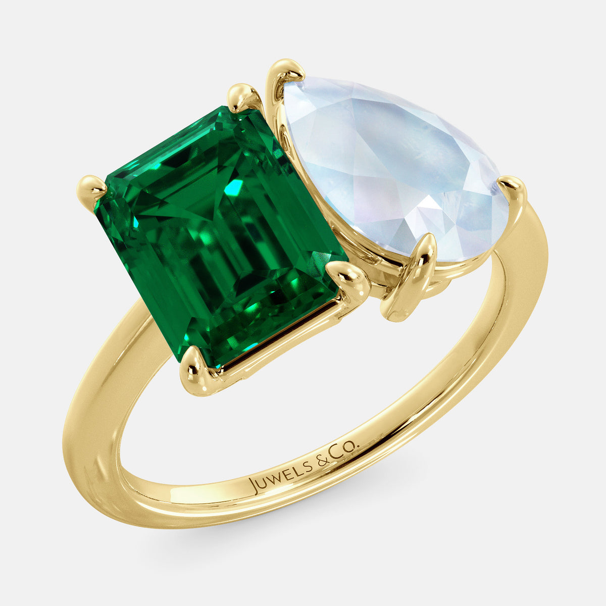 A toi et moi ring with an emerald-cut emerald and a pear-cut gemstone. The emerald-cut morganite is set on the left of the ring, and the pear-cut gemstone is set on the right. The ring is made of recycled yellow gold and has a simple, elegant design. The pear-cut gemstone can be customized. **Here are some additional details about the image:** * The emerald-cut white emerald is a birthstone for May. * The pear-cut gemstone can be customized to any stone of your choice.