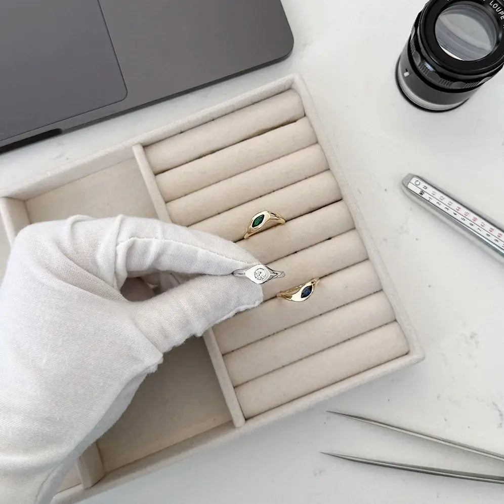 Jewelry box with rings, a gloved hand holding one, and a camera lens in the background.