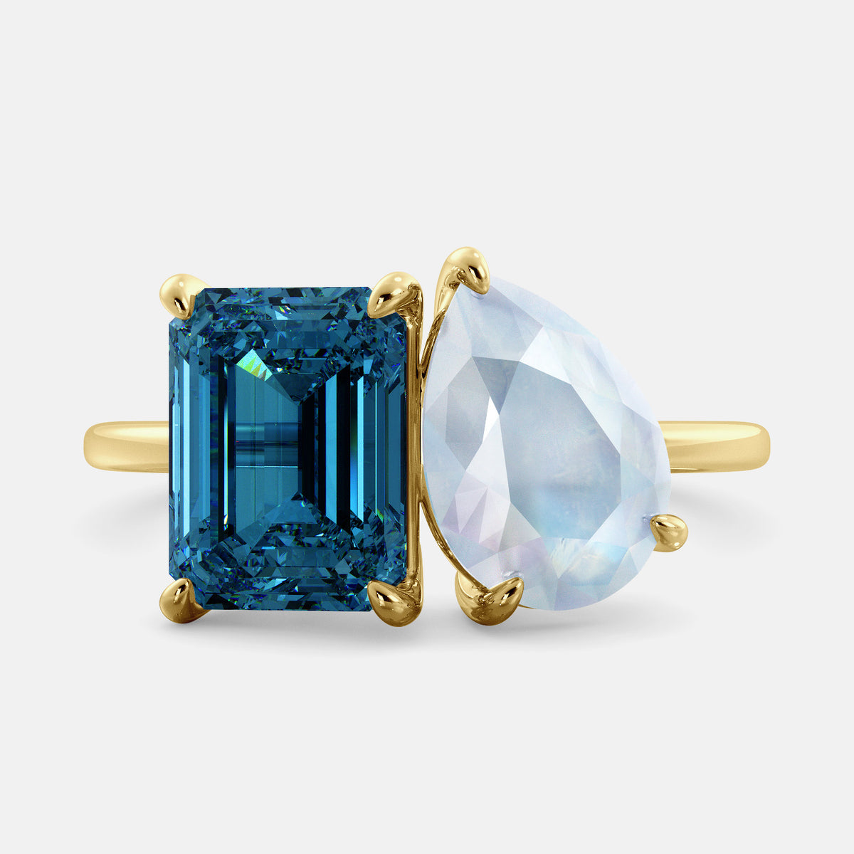A toi et moi ring with an emerald-cut London Blue Topaz and pear-cut gemstone. The emerald-cut morganite is set on the left of the ring, and the pear-cut gemstone is set on the right. The ring is made of recycled yellow gold and has a simple, elegant design. The pear-cut gemstone can be customized. **Here are some additional details about the image:** * The emerald-cut white London Blue Topaz is a birthstone for December. * The pear-cut gemstone can be customized to any stone of your choice.