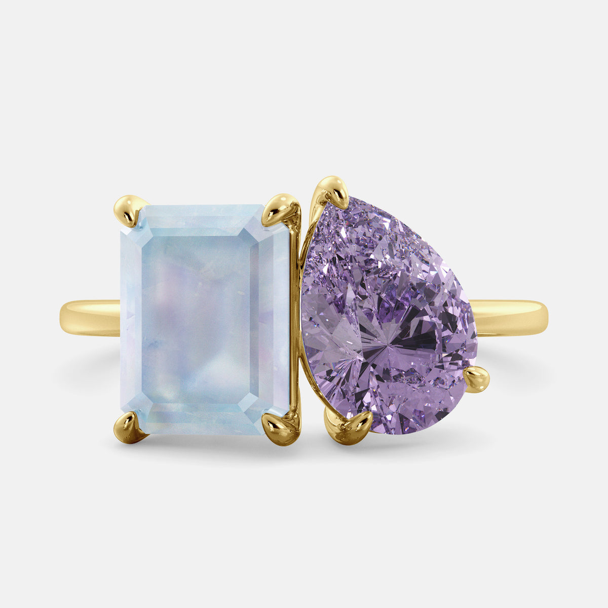 A toi et moi ring with an emerald-cut moonstone and a pear-cut gemstone. The emerald-cut is set on the left of the ring, and the pear-cut gemstone is set on the right. The ring is made of recycled yellow gold and has a simple, elegant design. The pear-cut gemstone can be customized. **Here are some additional details about the image:** * The emerald-cut white moonstone is a birthstone for June. * The pear-cut gemstone can be customized to any stone of your choice.