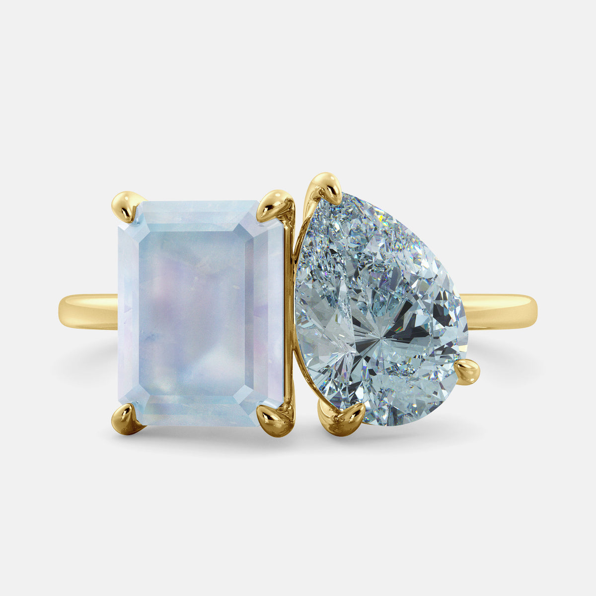 A toi et moi ring with an emerald-cut moonstone and a pear-cut gemstone. The emerald-cut morganite is set on the left of the ring, and the pear-cut gemstone is set on the right. The ring is made of recycled yellow gold and has a simple, elegant design. The pear-cut gemstone can be customized. **Here are some additional details about the image:** * The emerald-cut white moonstone is a birthstone for June. * The pear-cut gemstone can be customized to any stone of your choice.