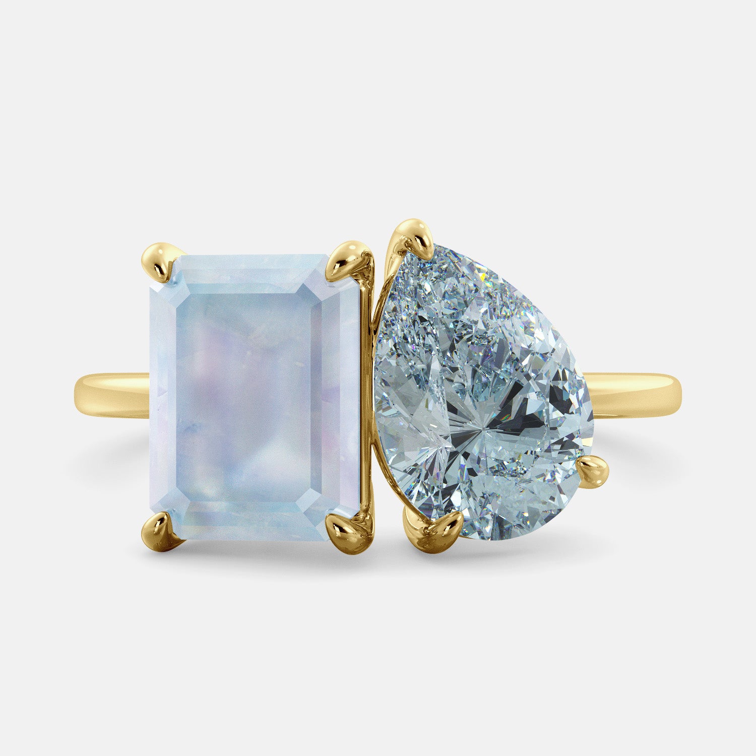 A toi et moi ring with an emerald-cut moonstone and a pear-cut gemstone. The emerald-cut morganite is set on the left of the ring, and the pear-cut gemstone is set on the right. The ring is made of recycled yellow gold and has a simple, elegant design. The pear-cut gemstone can be customized. **Here are some additional details about the image:** * The emerald-cut white moonstone is a birthstone for June. * The pear-cut gemstone can be customized to any stone of your choice.