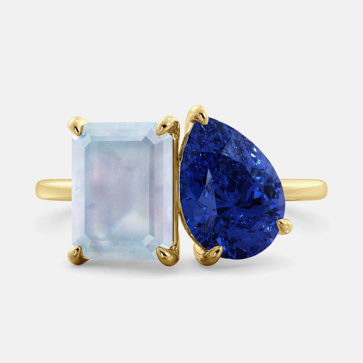 A toi et moi ring with an emerald-cut moonstone and a pear-cut gemstone. The emerald-cut is set on the left of the ring, and the pear-cut gemstone is set on the right. The ring is made of recycled yellow gold and has a simple, elegant design. The pear-cut gemstone can be customized. **Here are some additional details about the image:** * The emerald-cut white moonstone is a birthstone for June. * The pear-cut gemstone can be customized to any stone of your choice.