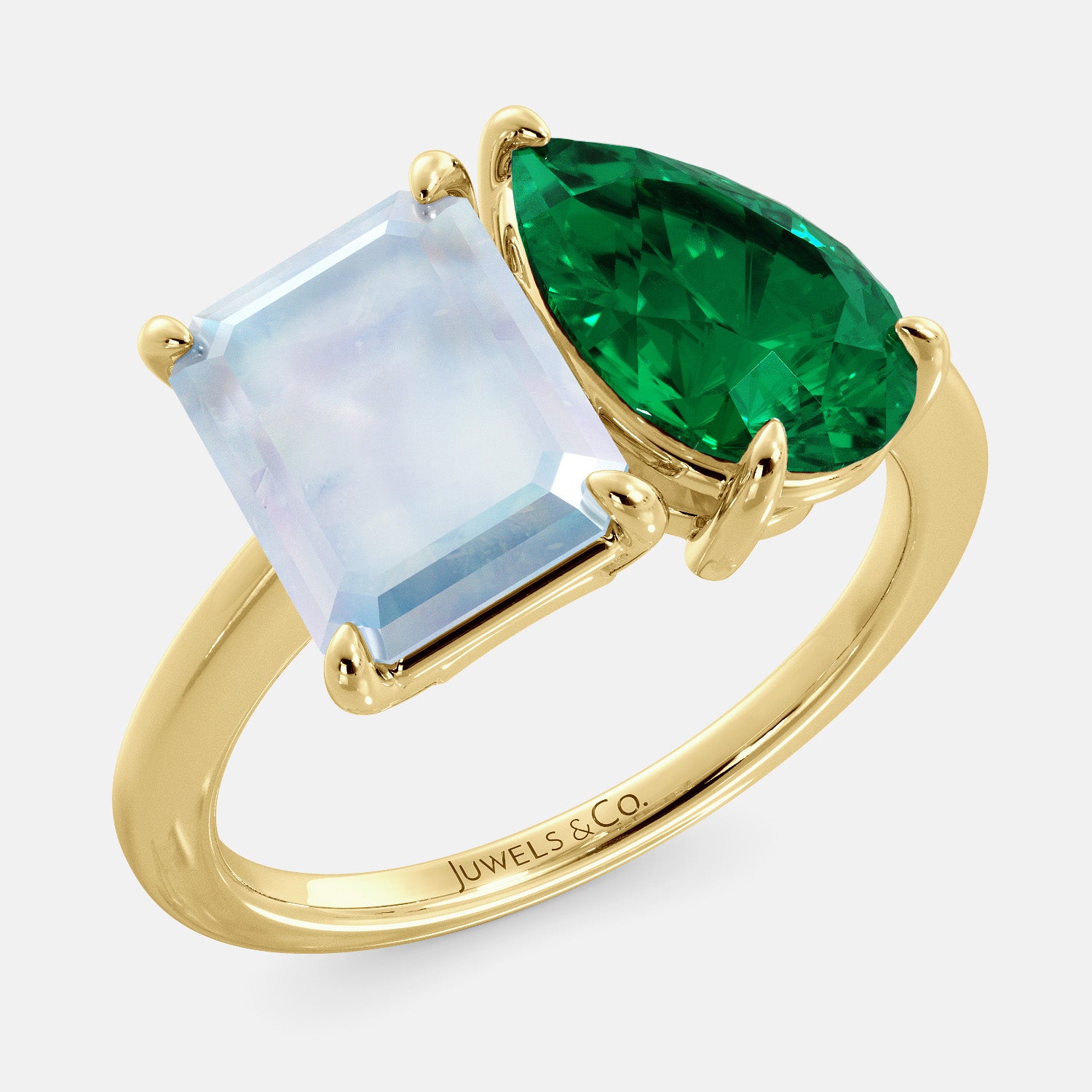 This image shows a toi et moi ring with a pear-shaped emerald and an emerald-cut moonstone. The ring is set in a 14k yellow gold band and is available in all sizes. The moonstone is a gemstone that is said to promote intuition, imagination, and creativity. The emerald is a gemstone that is said to promote love, compassion, and forgiveness. The toi et moi ring is a beautiful and unique way to show your love and commitment to someone special.