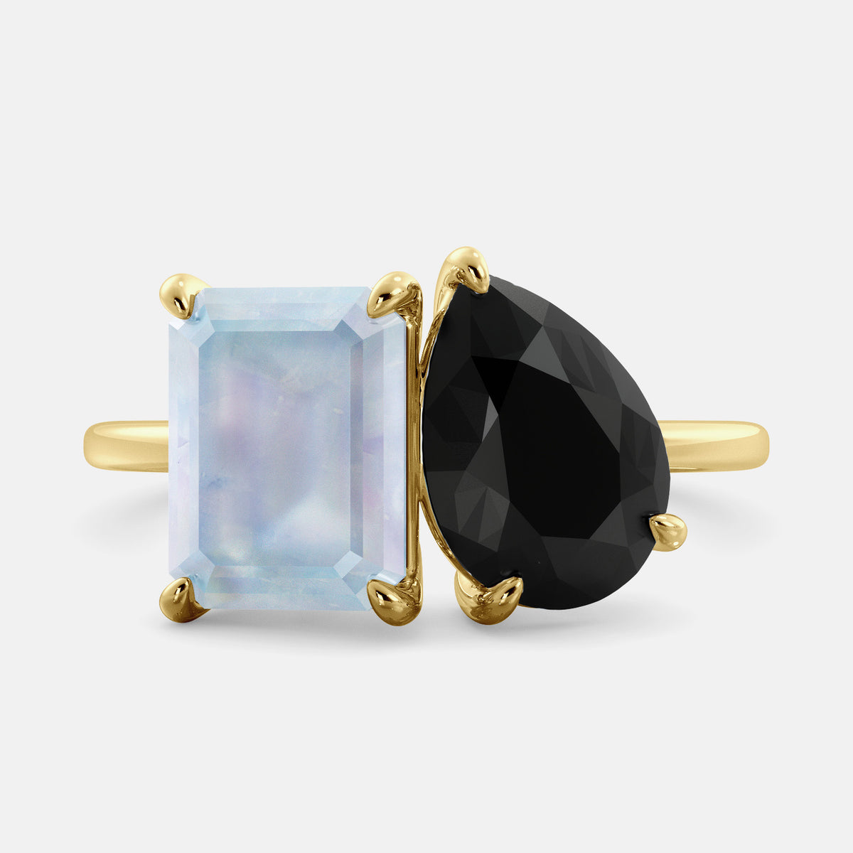 A toi et moi ring with one emerald cut moonstone and one pear cut onyx, set in 14k yellow gold. The moonstone is a soft blue-green color, and the ruby is a deep red. The two stones are set side by side, creating a beautiful contrast of colors. The ring is made of 14k yellow gold and has a polished finish. It is a perfect symbol of love and commitment.