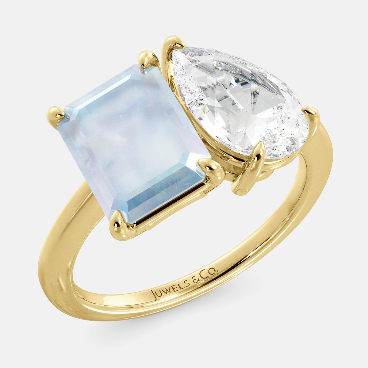 A toi et moi ring with an emerald-cut moonstone and a pear-cut gemstone. The emerald-cut morganite is set on the left of the ring, and the pear-cut gemstone is set on the right. The ring is made of recycled yellow gold and has a simple, elegant design. The pear-cut gemstone can be customized. **Here are some additional details about the image:** * The emerald-cut white moonstone is a birthstone for June. * The pear-cut gemstone can be customized to any stone of your choice.