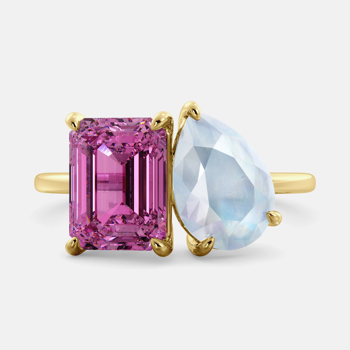 A toi et moi ring with an emerald-cut Pink Sapphire and pear-cut gemstone. The emerald-cut is set on the left of the ring, and the pear-cut gemstone is set on the right. The ring is made of recycled yellow gold and has a simple, elegant design. The pear-cut gemstone can be customized. **Here are some additional details about the image:** * The emerald-cut white Pink Sapphire is a birthstone for October. * The pear-cut gemstone can be customized to any stone of your choice.