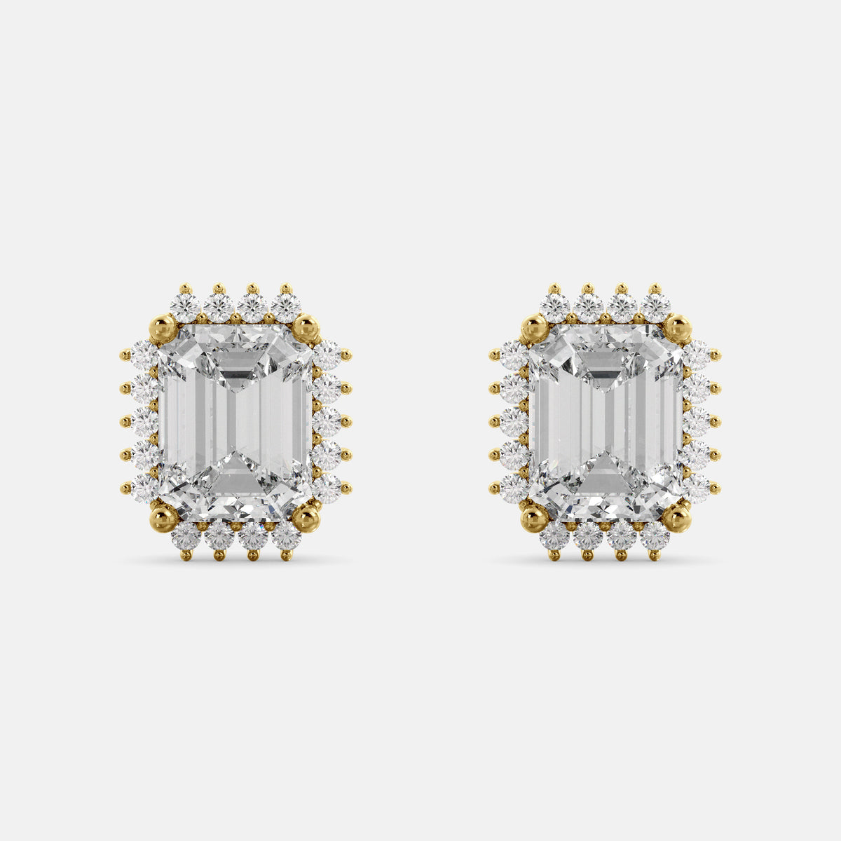 A pair of emerald-cut diamond earrings with halo designs, set in yellow gold.