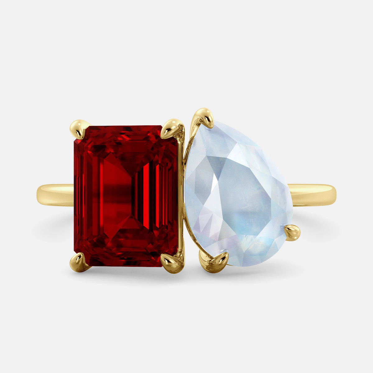 A toi et moi ring with an emerald-cut ruby and a pear-cut gemstone. The emerald-cut morganite is set on the left of the ring, and the pear-cut gemstone is set on the right. The ring is made of recycled yellow gold and has a simple, elegant design. The pear-cut gemstone can be customized. **Here are some additional details about the image:** * The emerald-cut white ruby is a birthstone for July. * The pear-cut gemstone can be customized to any stone of your choice.