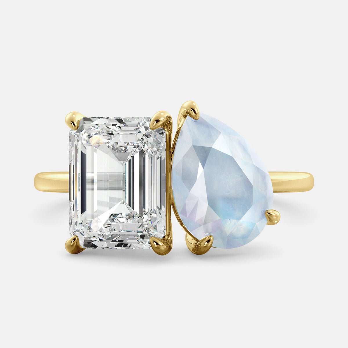 A toi et moi ring with an emerald-cut white topaz and a pear-cut gemstone. The emerald-cut morganite is set on the left of the ring, and the pear-cut gemstone is set on the right. The ring is made of recycled yellow gold and has a simple, elegant design. The pear-cut gemstone can be customized. **Here are some additional details about the image:** * The emerald-cut white topaz is a birthstone for April. * The pear-cut gemstone can be customized to any stone of your choice.