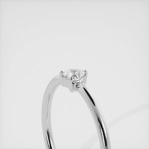A close-up of a heart-shaped solitaire diamond ring in recycled white gold. The ring is set with a single, large diamond in the center of a heart-shaped setting. The ring is made of recycled white gold and has a simple, elegant design. The diamond is sparkling and reflects light beautifully. The ring is a perfect gift for a loved one or a special occasion.