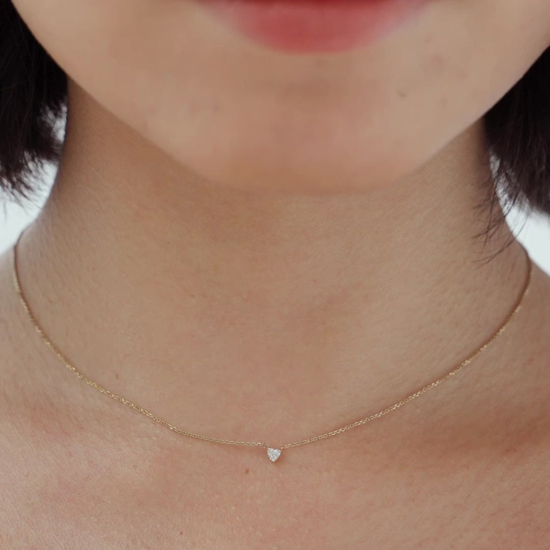 A close-up of a heart-shaped diamond necklace in recycled yellow gold. The necklace is set with a single heart-shaped diamond in the center of a pendant. The necklace is made of recycled yellow gold and has a simple, elegant design. The diamond is sparkling and reflects light beautifully. The necklace is a perfect gift for a loved one or a special occasion.