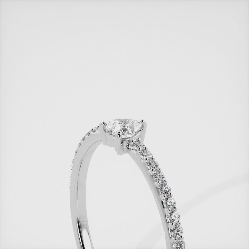 A close-up of a heart-shaped diamond ring with side stones in recycled white gold. The ring is set with a single, large diamond in the center of a heart-shaped setting. The ring is made of recycled yellow gold and has a simple, elegant design. The diamond is sparkling and reflects light beautifully. The side stones are smaller diamonds that are set in the band of the ring. The ring is a perfect gift for a loved one or a special occasion.