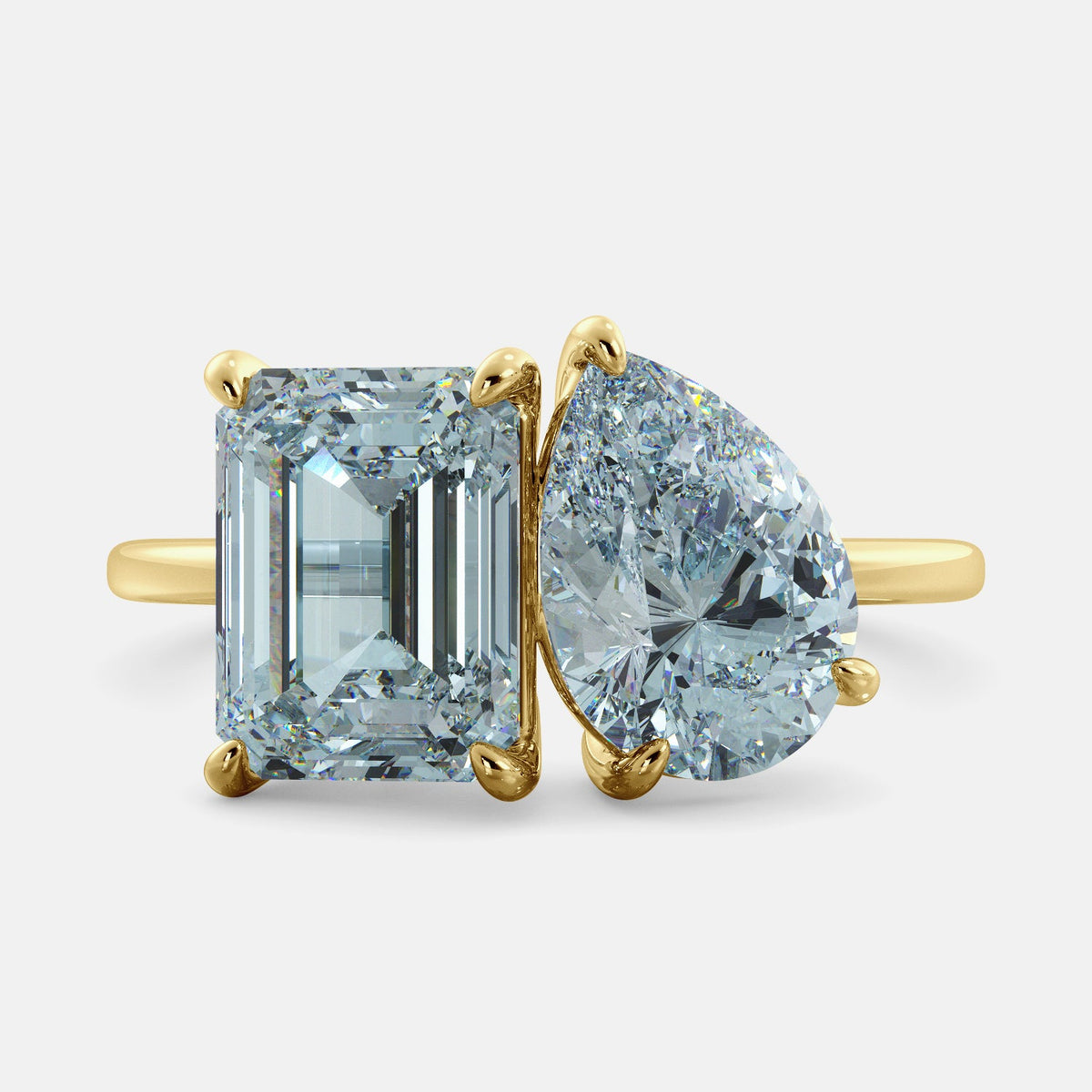 A toi et moi ring with an emerald-cut aquamarine and a pear-cut gemstone. The emerald-cut morganite is set on the left of the ring, and the pear-cut gemstone is set on the right. The ring is made of recycled yellow gold and has a simple, elegant design. The pear-cut gemstone can be customized. **Here are some additional details about the image:** * The emerald-cut aquamarine is a birthstone for March. * The pear-cut gemstone can be customized to any stone of your choice.
