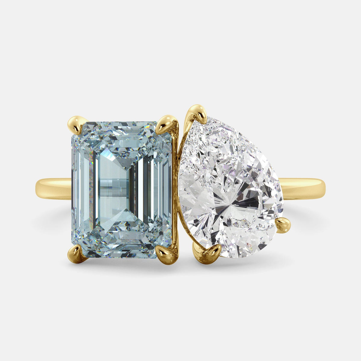 A toi et moi ring with an emerald-cut aquamarine and a pear-cut gemstone. The emerald-cut morganite is set on the left of the ring, and the pear-cut gemstone is set on the right. The ring is made of recycled yellow gold and has a simple, elegant design. The pear-cut gemstone can be customized. **Here are some additional details about the image:** * The emerald-cut aquamarine is a birthstone for March. * The pear-cut gemstone can be customized to any stone of your choice.