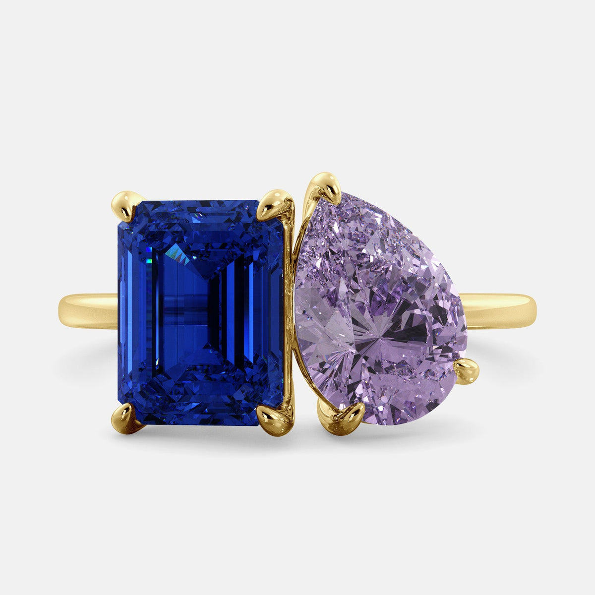 A toi et moi ring with an emerald-cut Blue Sapphire and pear-cut gemstone. The emerald-cut morganite is set on the left of the ring, and the pear-cut gemstone is set on the right. The ring is made of recycled yellow gold and has a simple, elegant design. The pear-cut gemstone can be customized. **Here are some additional details about the image:** * The emerald-cut white Blue Sapphire is a birthstone for September. * The pear-cut gemstone can be customized to any stone of your choice.