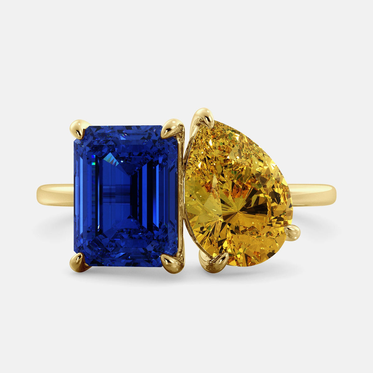 A toi et moi ring with an emerald-cut Blue Sapphire and pear-cut gemstone. The emerald-cut morganite is set on the left of the ring, and the pear-cut gemstone is set on the right. The ring is made of recycled yellow gold and has a simple, elegant design. The pear-cut gemstone can be customized. **Here are some additional details about the image:** * The emerald-cut white Blue Sapphire is a birthstone for September. * The pear-cut gemstone can be customized to any stone of your choice.