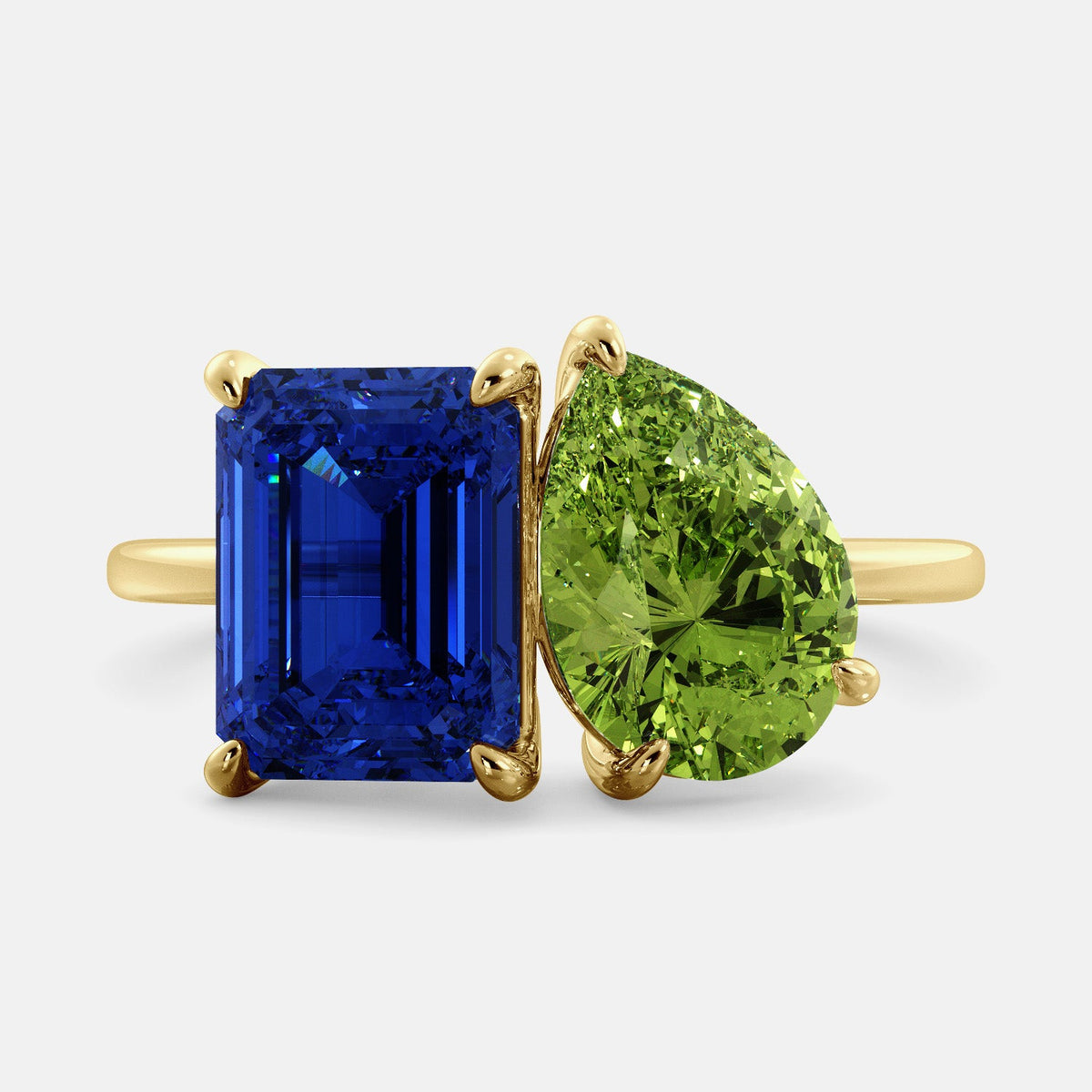A toi et moi ring with an emerald-cut Blue Sapphire and pear-cut gemstone. The emerald-cut morganite is set on the left of the ring, and the pear-cut gemstone is set on the right. The ring is made of recycled yellow gold and has a simple, elegant design. The pear-cut gemstone can be customized. **Here are some additional details about the image:** * The emerald-cut white Blue Sapphire is a birthstone for September. * The pear-cut gemstone can be customized to any stone of your choice.