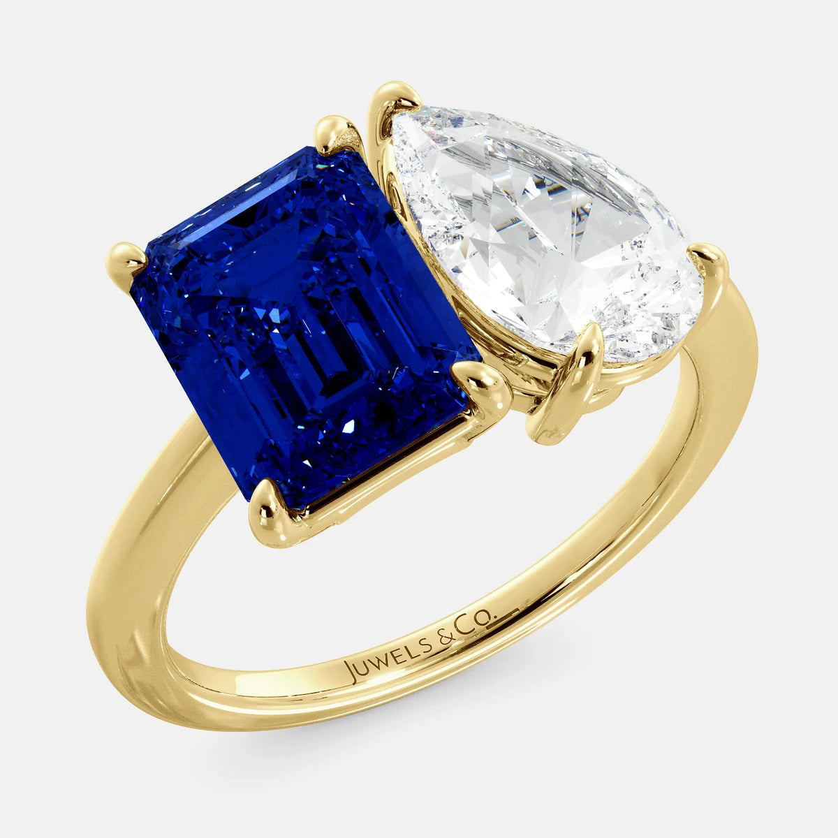 This image shows a toi et moi ring with a pear-shaped white topaz and an emerald-cut blue sapphire. The ring is set in a 14k yellow gold band and is available in all sizes. The blue sapphire is a precious gemstone that is said to promote loyalty, wisdom, and truth. The white topaz is a clear, colorless stone that is said to promote creativity, imagination, and self-expression. The toi et moi ring is a beautiful and unique way to show your love and commitment to someone special.