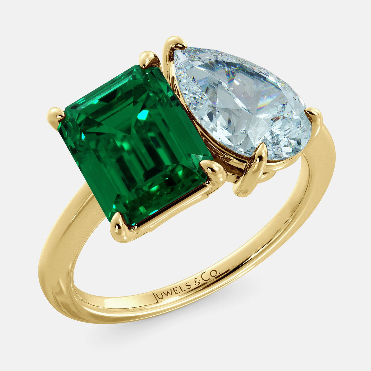 A toi et moi ring with an emerald-cut emerald and a pear-cut gemstone. The emerald-cut morganite is set on the left of the ring, and the pear-cut gemstone is set on the right. The ring is made of recycled yellow gold and has a simple, elegant design. The pear-cut gemstone can be customized. **Here are some additional details about the image:** * The emerald-cut white emerald is a birthstone for May. * The pear-cut gemstone can be customized to any stone of your choice.