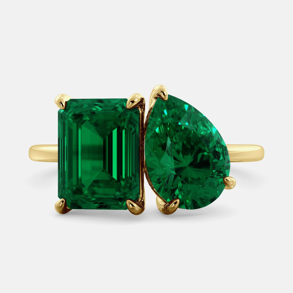 A toi et moi ring with an emerald-cut emerald and a pear-cut gemstone. The emerald-cut morganite is set on the left of the ring, and the pear-cut gemstone is set on the right. The ring is made of recycled yellow gold and has a simple, elegant design. The pear-cut gemstone can be customized. **Here are some additional details about the image:** * The emerald-cut white emerald is a birthstone for May. * The pear-cut gemstone can be customized to any stone of your choice.