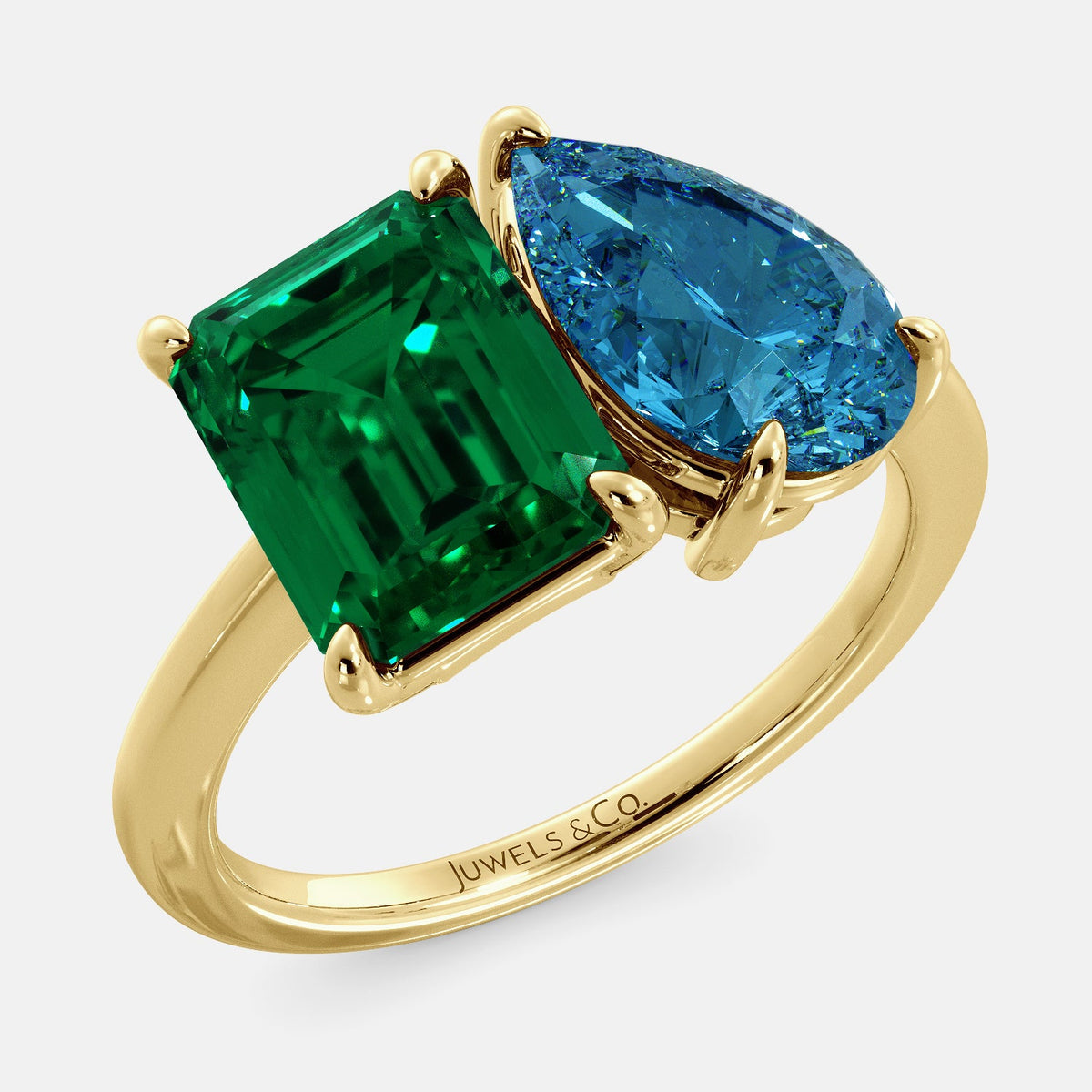 A toi et moi ring with an emerald-cut emerald and a pear-cut gemstone. The emerald-cut morganite is set on the left of the ring, and the pear-cut gemstone is set on the right. The ring is made of recycled yellow gold and has a simple, elegant design. The pear-cut gemstone can be customized. **Here are some additional details about the image:** * The emerald-cut white emerald is a birthstone for May. * The pear-cut gemstone can be customized to any stone of your choice.