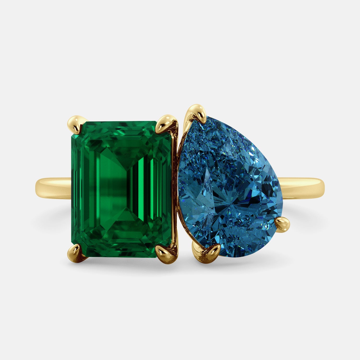 A toi et moi ring with an emerald-cut emerald and a pear-cut gemstone. The emerald-cut morganite is set on the left of the ring, and the pear-cut gemstone is set on the right. The ring is made of recycled yellow gold and has a simple, elegant design. The pear-cut gemstone can be customized. **Here are some additional details about the image:** * The emerald-cut white emerald is a birthstone for May. * The pear-cut gemstone can be customized to any stone of your choice.