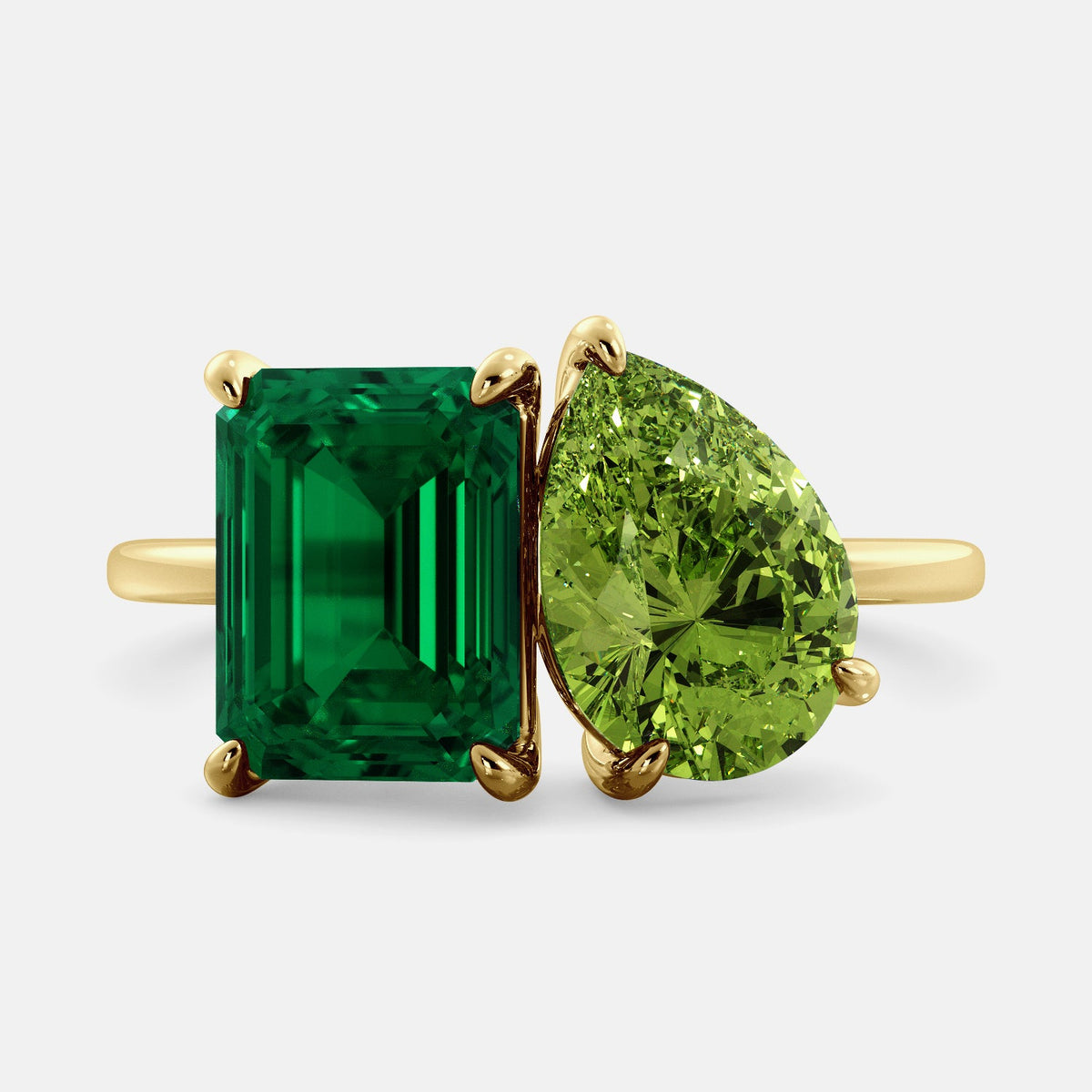 A toi et moi ring with an emerald-cut emerald and a pear-cut gemstone. The emerald-cut morganite is set on the left of the ring, and the pear-cut gemstone is set on the right. The ring is made of recycled yellow gold and has a simple, elegant design. The pear-cut gemstone can be customized. **Here are some additional details about the image:** * The emerald-cut white emerald is a birthstone for May. * The pear-cut gemstone can be customized to any stone of your choice.