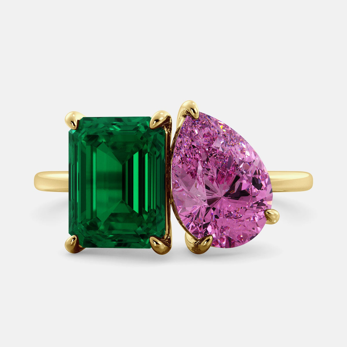 A toi et moi ring with an emerald-cut emerald and a pear-cut gemstone. The emerald-cut morganite is set on the left of the ring, and the pear-cut gemstone is set on the right. The ring is made of recycled yellow gold and has a simple, elegant design. The pear-cut gemstone can be customized. **Here are some additional details about the image:** * The emerald-cut white emerald is a birthstone for May. * The pear-cut gemstone can be customized to any stone of your choice.