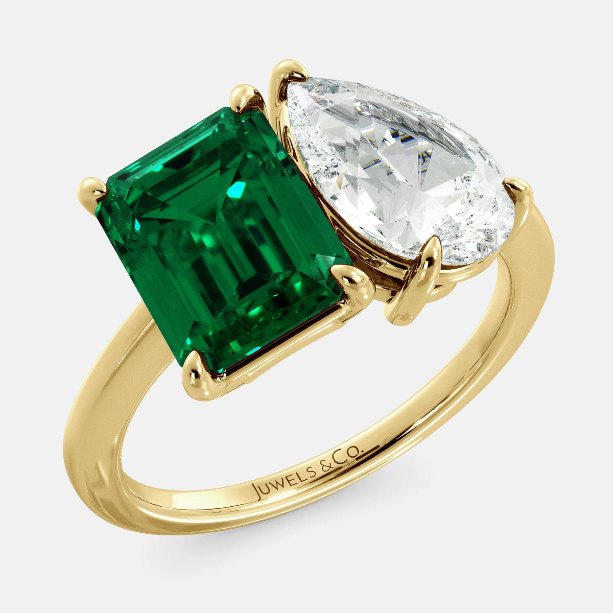 A toi et moi ring with an emerald-cut emerald and a pear-cut gemstone. The emerald-cut morganite is set on the left of the ring, and the pear-cut gemstone is set on the right. The ring is made of recycled yellow gold and has a simple, elegant design. The pear-cut gemstone can be customized. **Here are some additional details about the image:** * The emerald-cut white emerald is a birthstone for May. * The pear-cut gemstone can be customized to any stone of your choice.