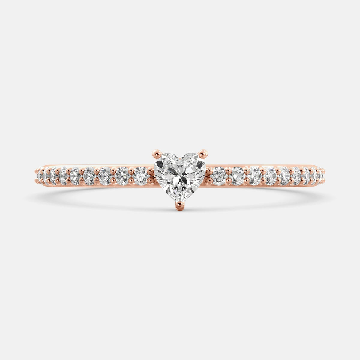 A close-up of a heart-shaped diamond ring with side stones in recycled rose gold. The ring is set with a single, large diamond in the center of a heart-shaped setting. The ring is made of recycled yellow gold and has a simple, elegant design. The diamond is sparkling and reflects light beautifully. The side stones are smaller diamonds that are set in the band of the ring. The ring is a perfect gift for a loved one or a special occasion.
