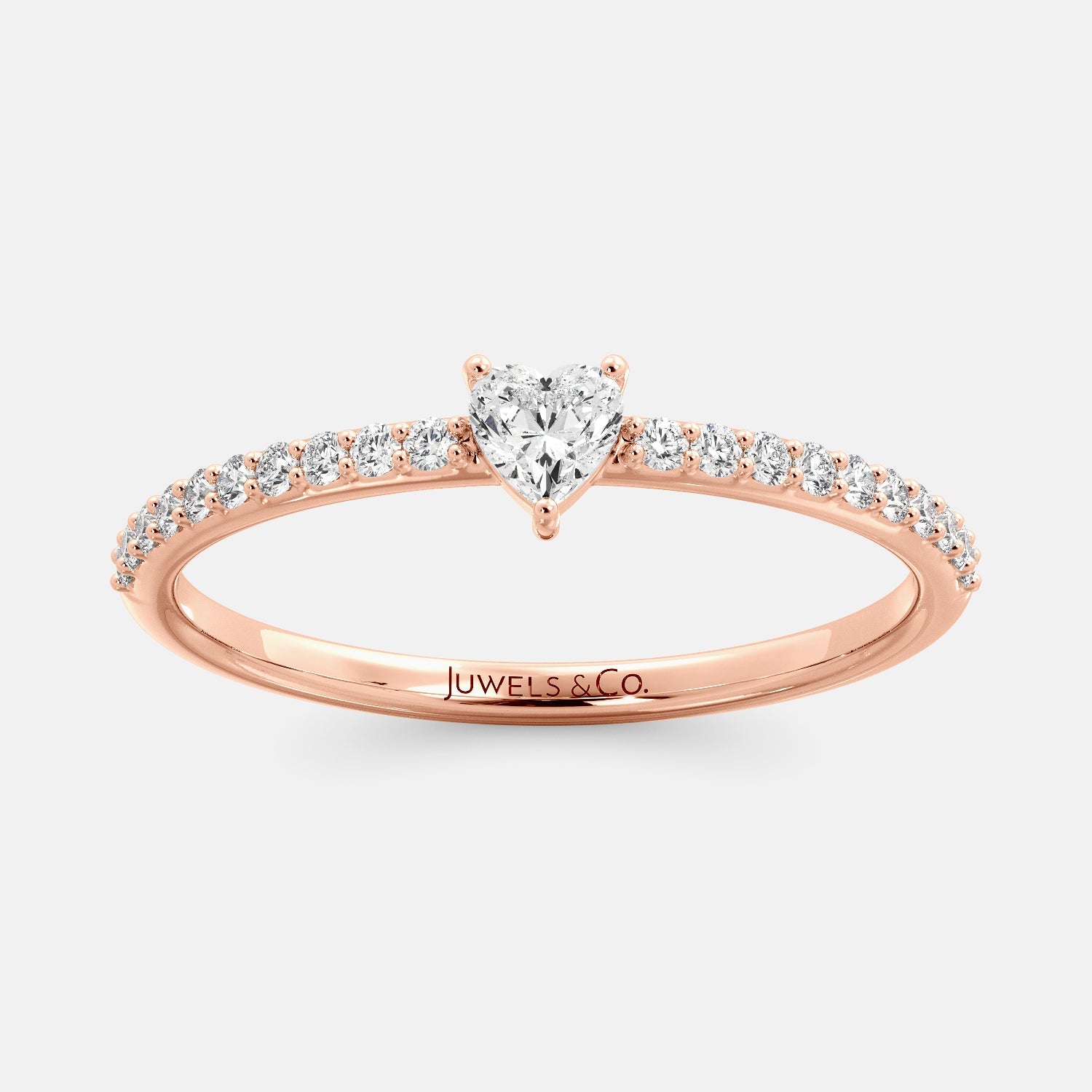 A close-up of a heart-shaped diamond ring with side stones in recycled rose gold. The ring is set with a single, large diamond in the center of a heart-shaped setting. The ring is made of recycled yellow gold and has a simple, elegant design. The diamond is sparkling and reflects light beautifully. The side stones are smaller diamonds that are set in the band of the ring. The ring is a perfect gift for a loved one or a special occasion.