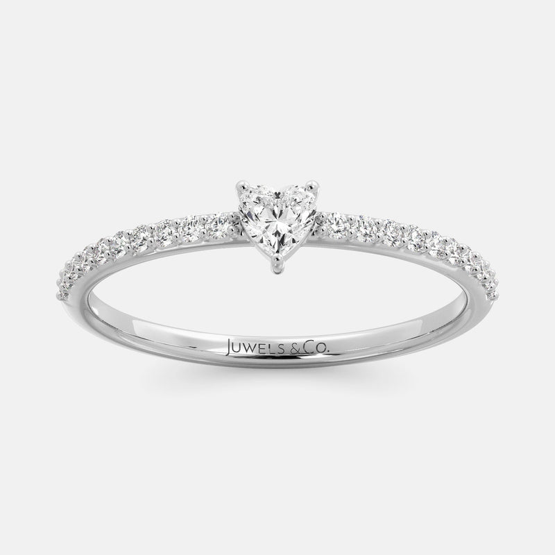 A close-up of a heart-shaped diamond ring with side stones in recycled white gold. The ring is set with a single, large diamond in the center of a heart-shaped setting. The ring is made of recycled yellow gold and has a simple, elegant design. The diamond is sparkling and reflects light beautifully. The side stones are smaller diamonds that are set in the band of the ring. The ring is a perfect gift for a loved one or a special occasion.