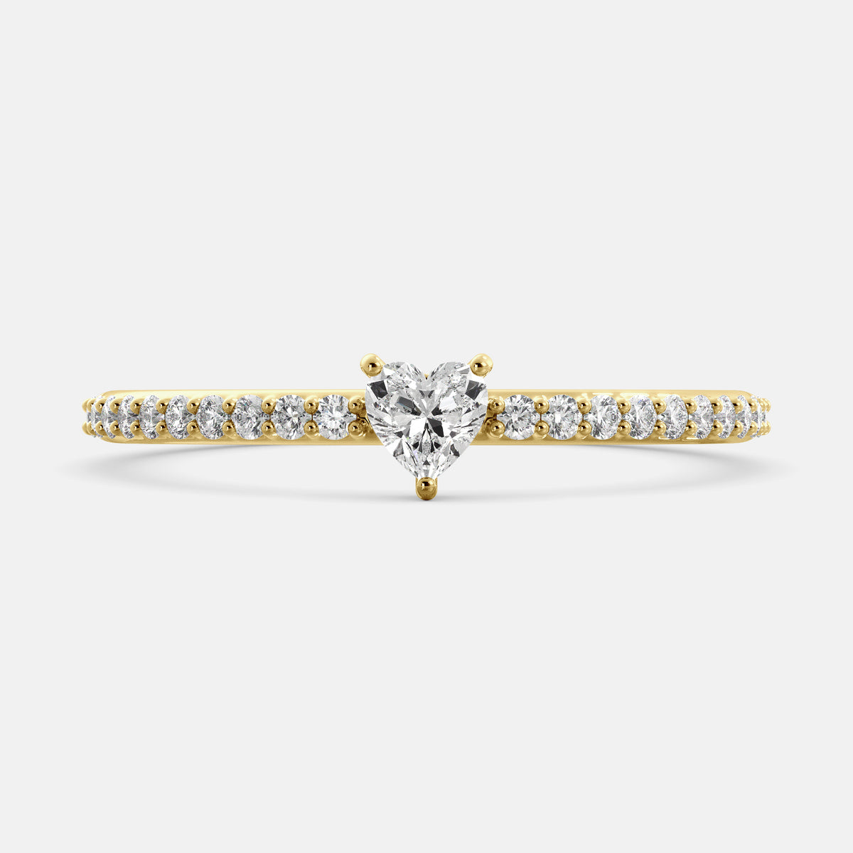A close-up of a heart-shaped diamond ring with side stones in recycled yellow gold. The ring is set with a single, large diamond in the center of a heart-shaped setting. The ring is made of recycled yellow gold and has a simple, elegant design. The diamond is sparkling and reflects light beautifully. The side stones are smaller diamonds that are set in the band of the ring. The ring is a perfect gift for a loved one or a special occasion.