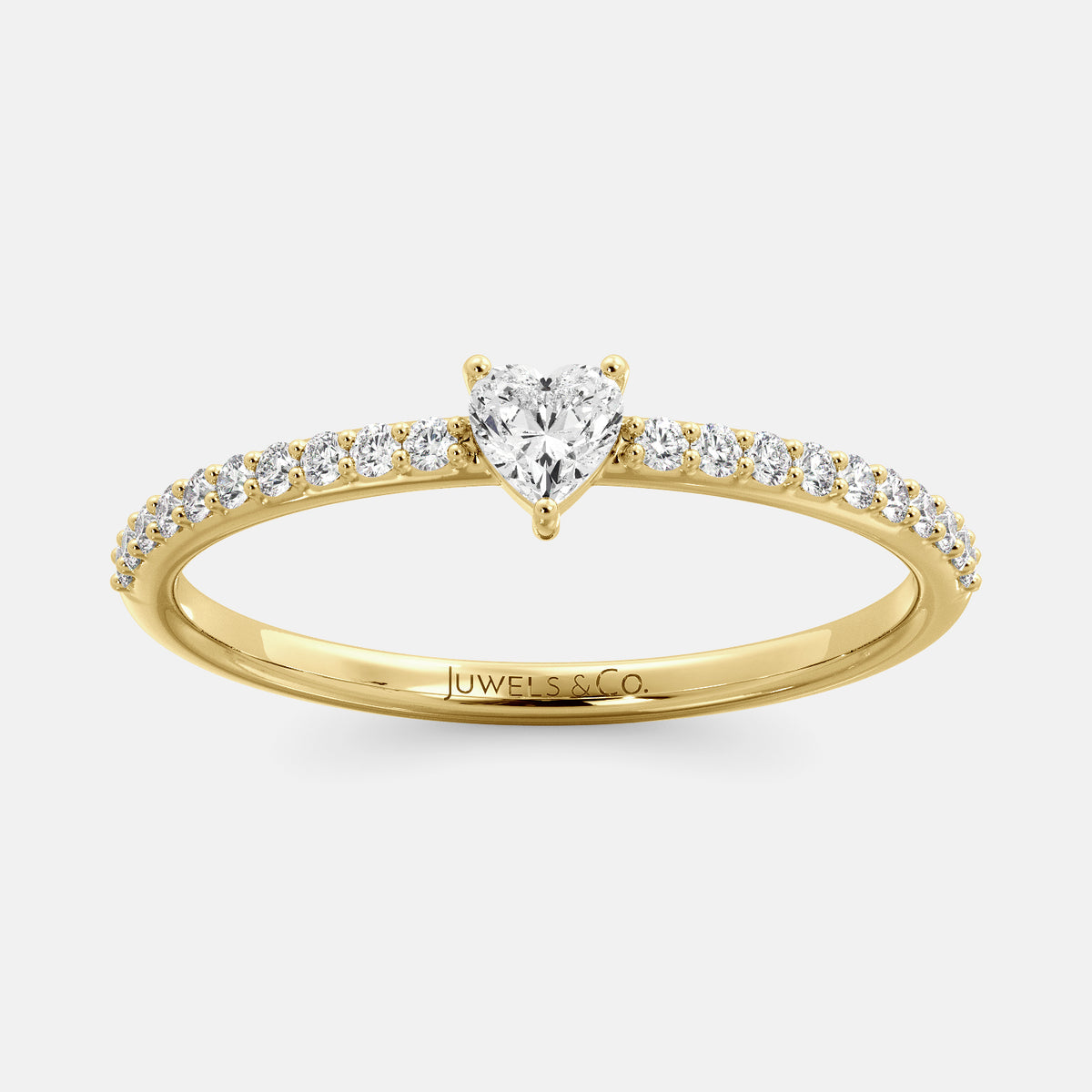 A close-up of a heart-shaped diamond ring with side stones in recycled yellow gold. The ring is set with a single, large diamond in the center of a heart-shaped setting. The ring is made of recycled yellow gold and has a simple, elegant design. The diamond is sparkling and reflects light beautifully. The side stones are smaller diamonds that are set in the band of the ring. The ring is a perfect gift for a loved one or a special occasion
