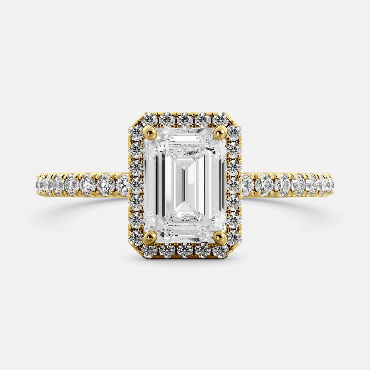 This image shows a stunning emerald halo lab-grown diamond ring with pavé on a yellow gold band. The ring features a 1.5-carat emerald-cut lab-grown diamond in the center, surrounded by a halo of smaller lab-grown diamonds. The ring is made of 14k yellow gold and is available in a variety of sizes.