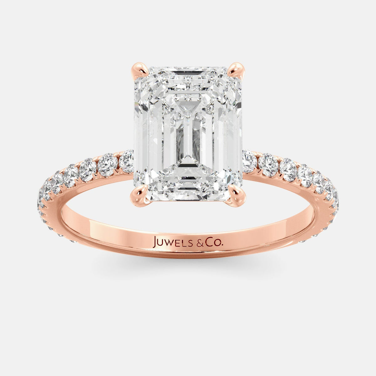 A close-up of an emerald solitaire lab-diamond ring with pave in rose gold. The ring is set with an emerald-cut lab diamond in the center, surrounded by a row of smaller diamonds on the band. The diamond is climate-positive as it used carbon from the atmosphere to produce. The ring is available in a variety of sizes and starts at \\$6,350.00.